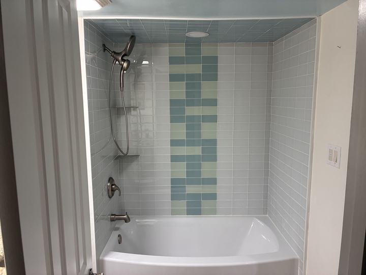 Glass subway tile tub surround with accent stripe and tiled ceiling
